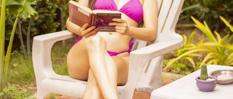 A person sitting on a white plastic chair outdoors, reading a book.