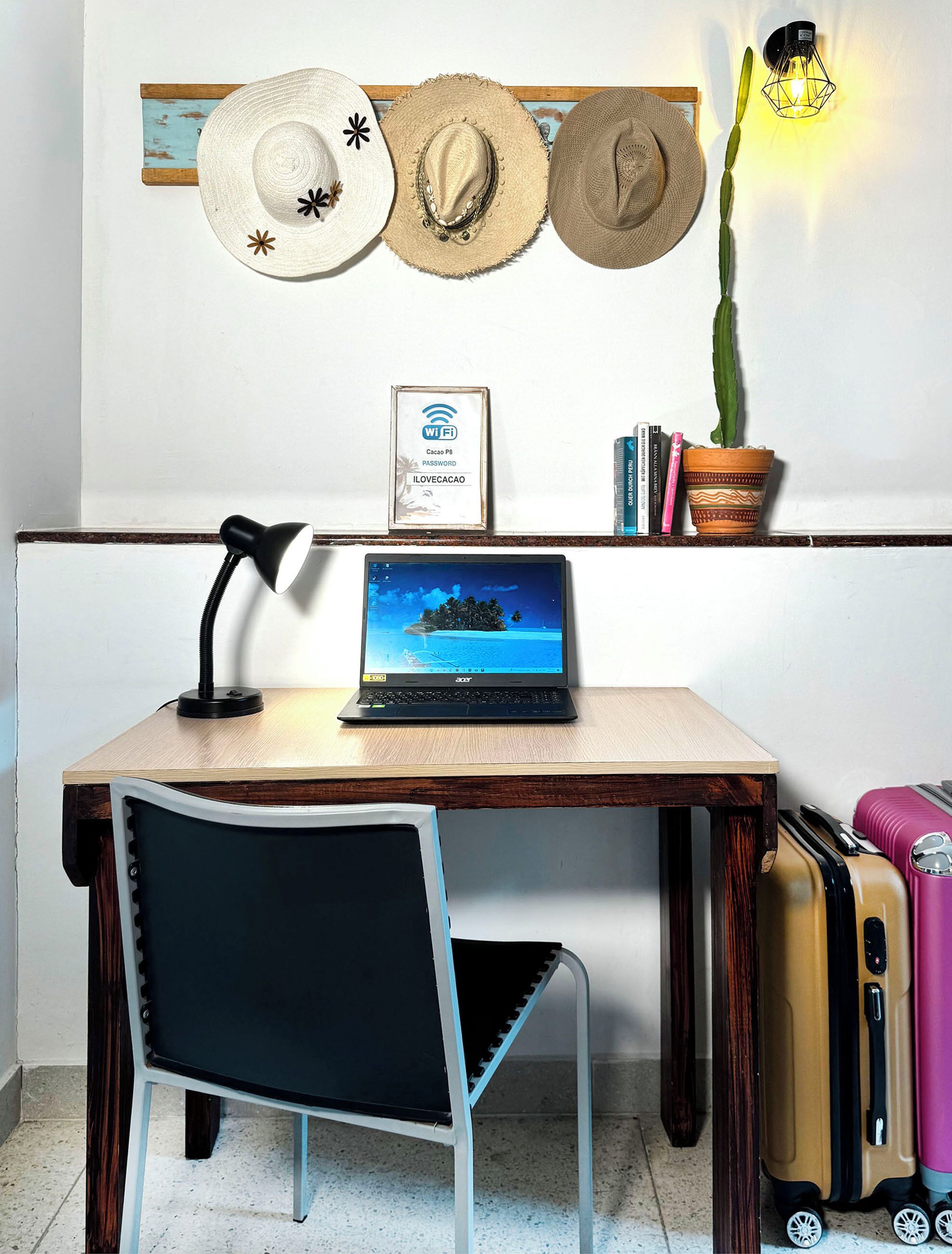 Uma mesa com um laptop, uma cadeira, um abajur, um vaso de planta e um aplique de parede.