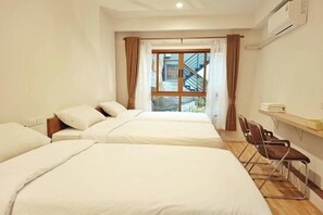 Une chambre d’hôtel avec deux lits, une fenêtre avec des rideaux, un bureau avec une chaise et un appareil de climatisation.