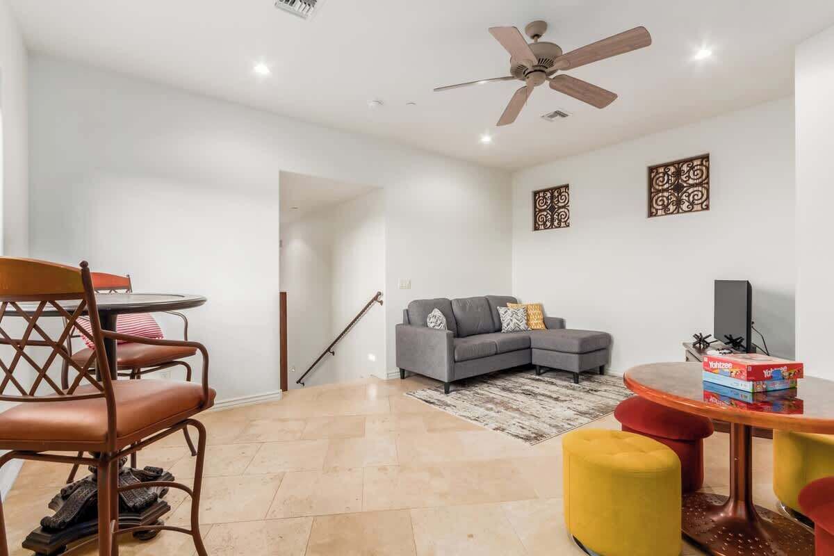 A modern living room with a sofa, a dining table with chairs, a ceiling fan, and a staircase.