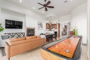 A spacious living area with a pool table, a leather sofa, and a ceiling fan.
