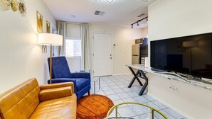 Un espace de vie compact comprenant un canapé, un fauteuil bleu, un téléviseur et un coin repas.