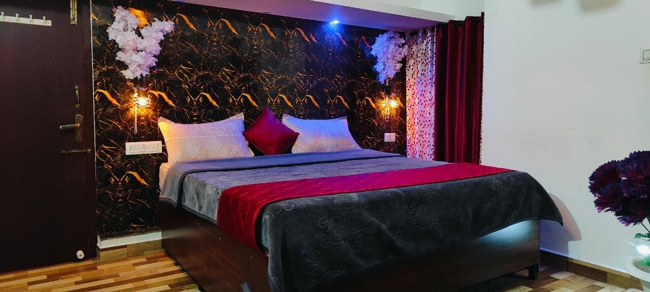 A bedroom with a bed, dark wood flooring, a marble-patterned wall, and a red curtain.