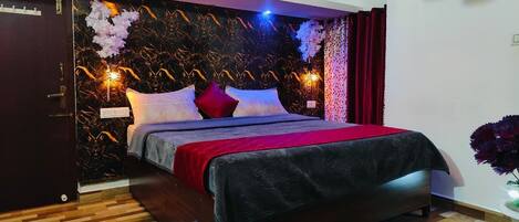 A bedroom with a bed, dark wood flooring, a marble-patterned wall, and a red curtain.
