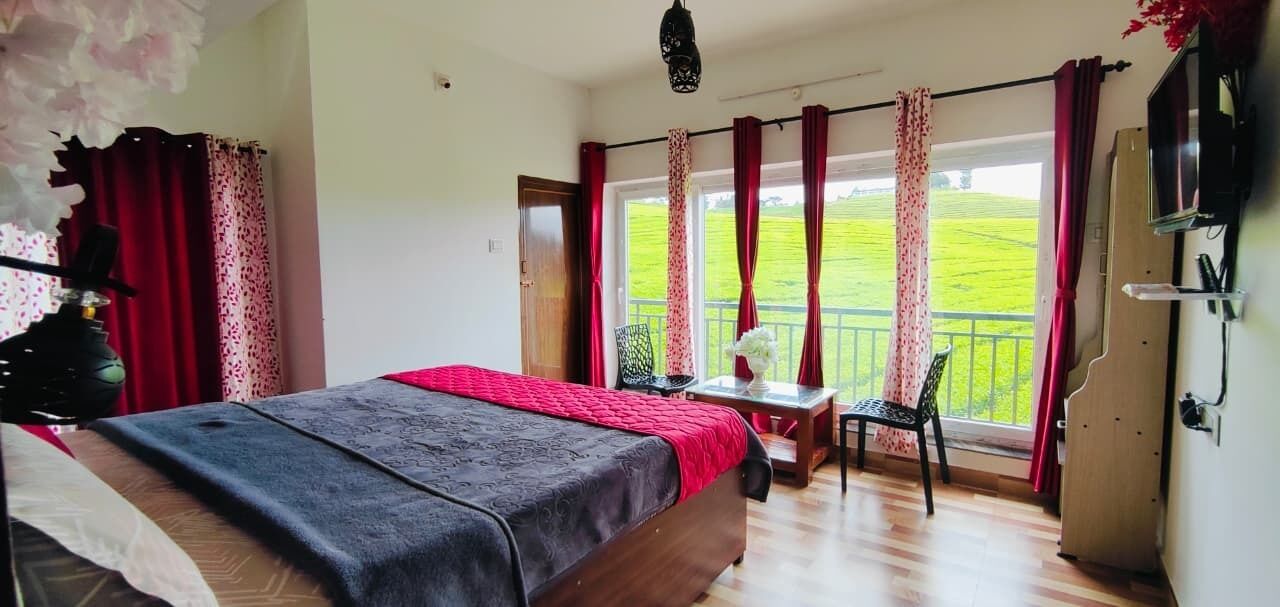 A bedroom with a bed, a desk, and a view of a green field through large windows.