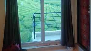 A room with a large window offering a view of a green field. - Tea Garden stays (Ooty)