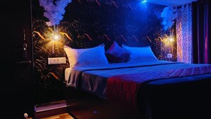 A dimly lit room with a bed, a nightstand, and a wall with decorative elements. - Tea Garden stays (Ooty)