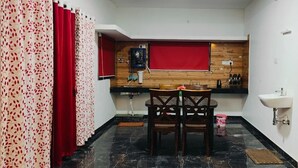 A compact kitchen with a dining table and chairs, a sink, and a wooden wall panel. - Tea Garden stays (Ooty)