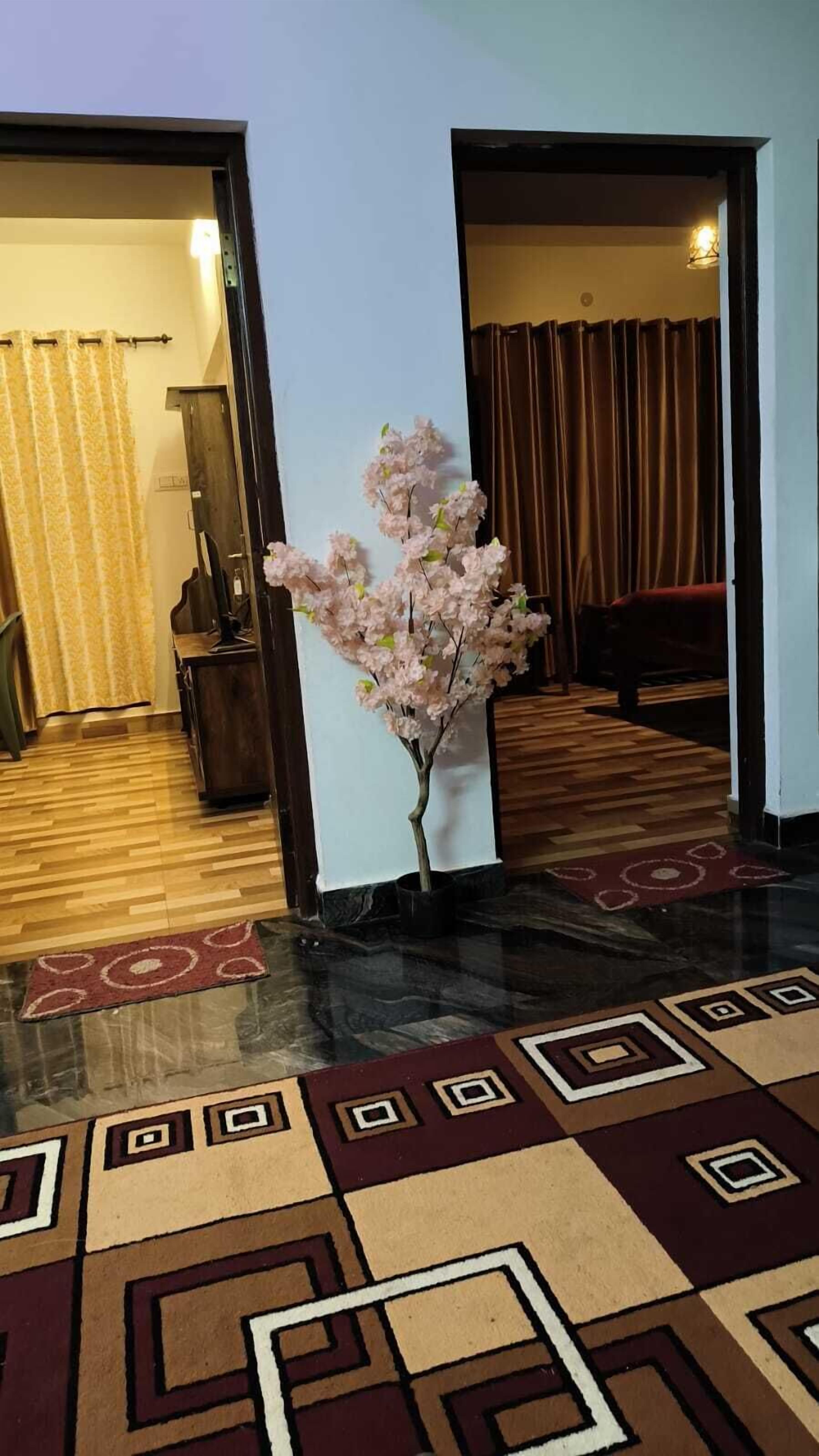 A hotel lobby with a central artificial cherry blossom tree, a patterned carpet, and a wooden floor.