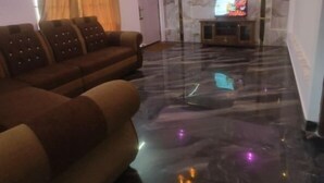 A living room with a marble floor, a sofa set, a television, and a ceiling light fixture. - Tea Garden stays (Ooty)