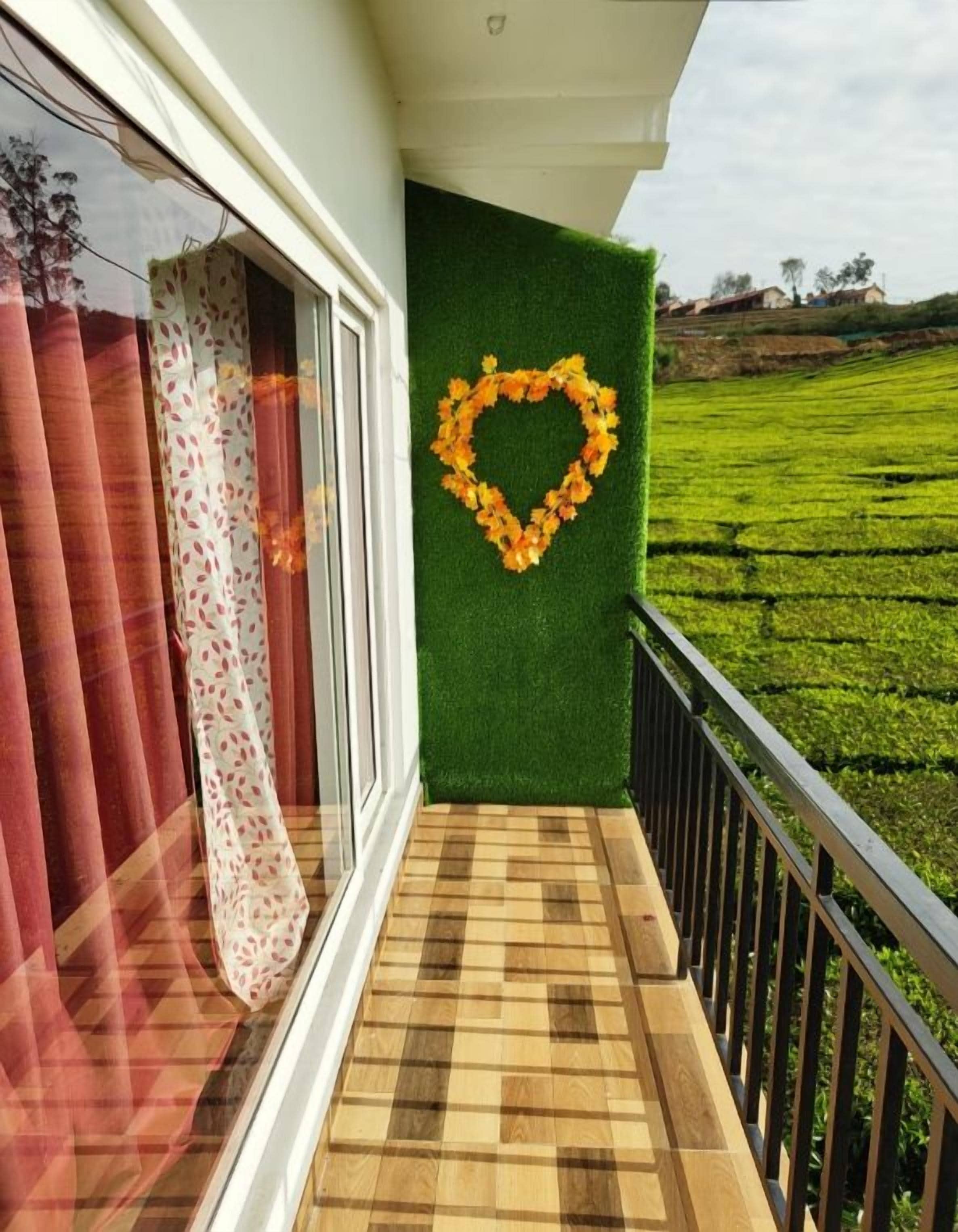 Un balcon doté d’un plancher en bois, une porte vitrée avec des rideaux rouges et un mur vert orné d’un motif en forme de cœur.