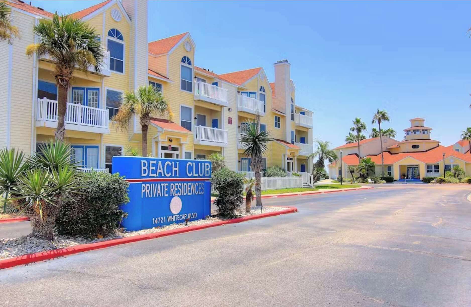 Ein Strandhotel mit Schild, das Privatwohnungen kennzeichnet, zeigt ein mehrgeschossiges Gebäude mit Balkonen und bewölktem Himmel.