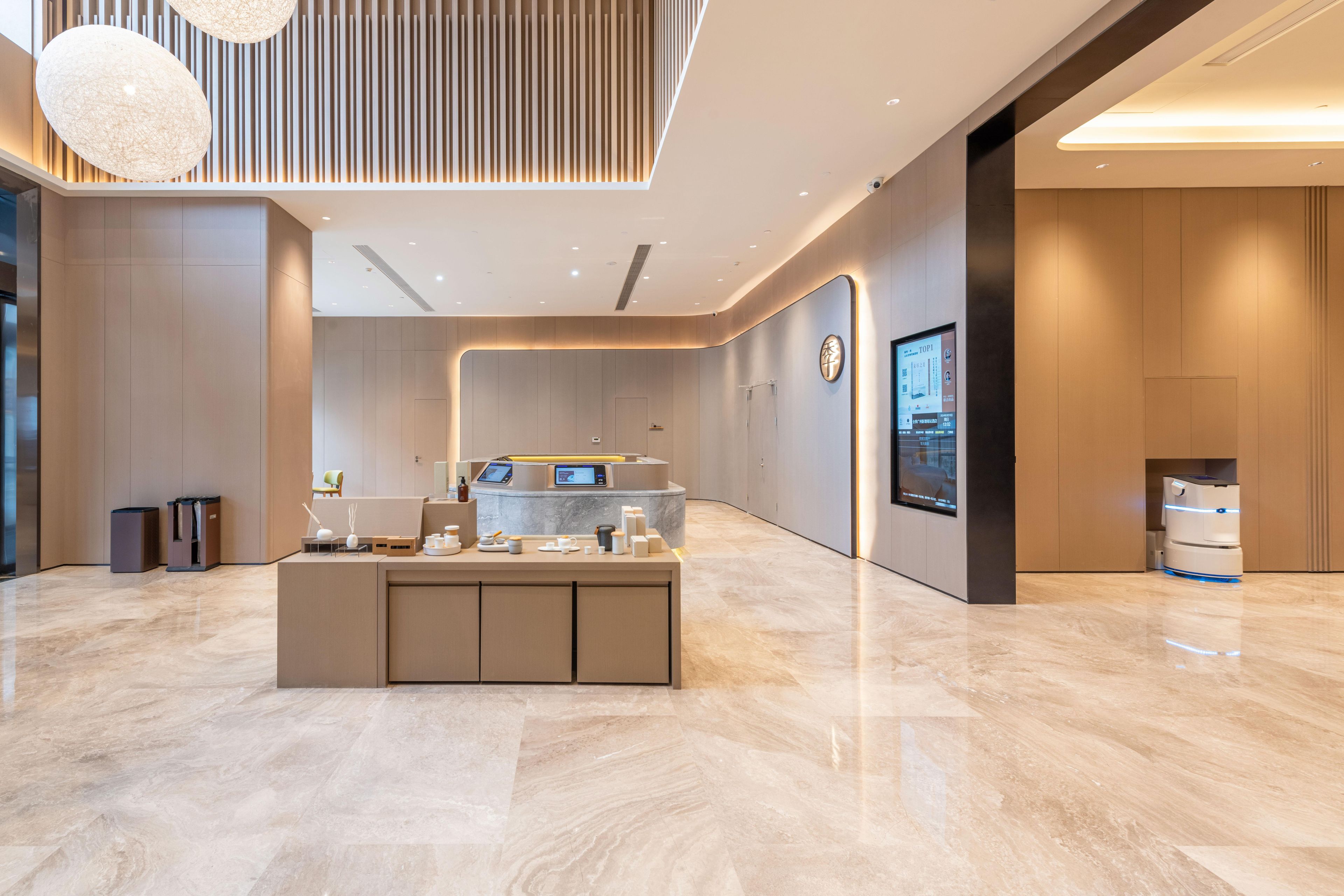A modern reception area with a marble floor, a central counter with a digital display, and a large screen on the wall.