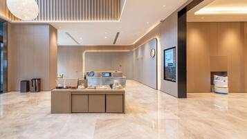 A modern reception area with a marble floor, a central counter with a digital display, and a large screen on the wall.