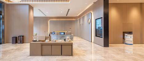 A modern reception area with a marble floor, a central counter with a digital display, and a large screen on the wall.