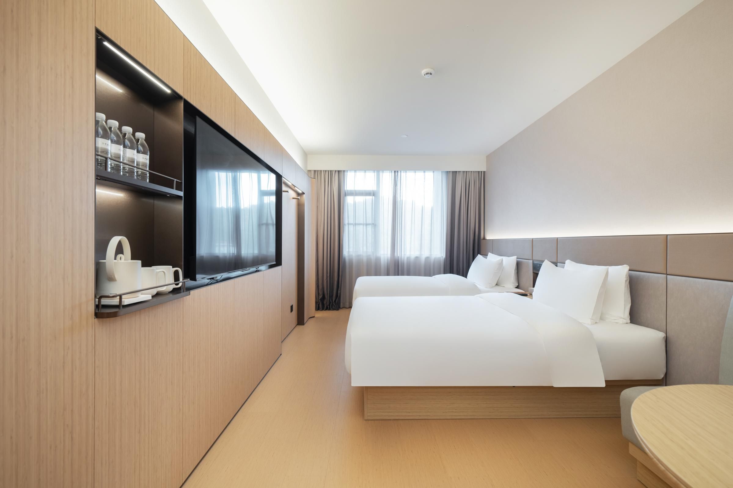 A hotel room with a bed, a TV, a minibar, and a window with curtains.