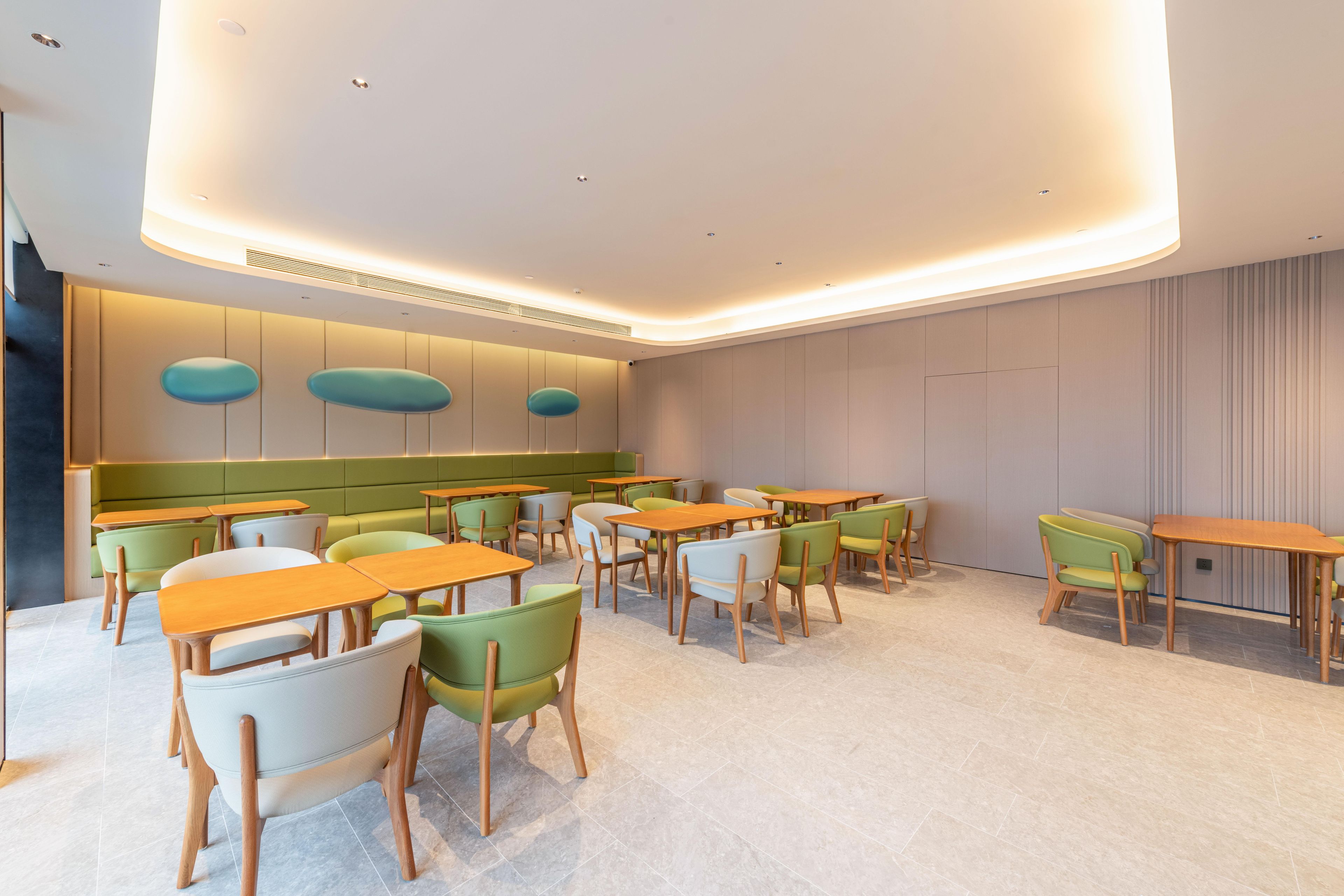 A modern dining area with multiple tables and chairs, a curved ceiling with recessed lighting, and a green accent wall.