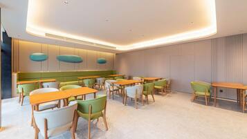 A modern dining area with multiple tables and chairs, a curved ceiling with recessed lighting, and a green accent wall.