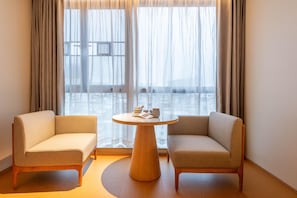 A modern room with two sofas facing a round wooden table, a large window with sheer curtains, and a view of a cityscape. - Ji Hotel Guangzhou Xintang South Station (Guangzhou)