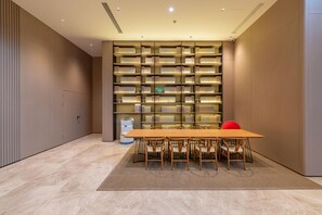A modern library with a long wooden table and chairs, surrounded by bookshelves. - Ji Hotel Guangzhou Xintang South Station (Guangzhou)