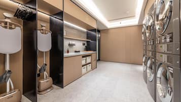 A modern laundry room with multiple washing machines, a folding station, and a mirror.