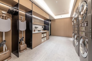 A modern laundry room with multiple washing machines, a folding station, and a mirror. - Ji Hotel Guangzhou Xintang South Station (Guangzhou)