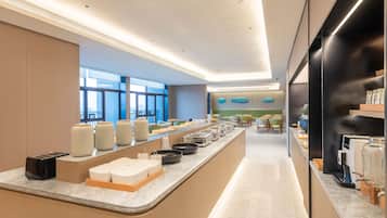 A modern hotel lobby with a long reception counter, seating area, and large windows.