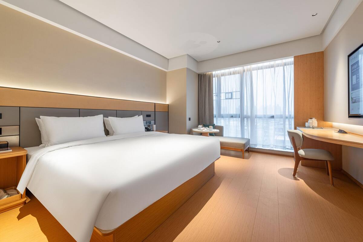 A modern hotel room with a large bed, a desk, and a chair.