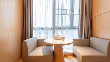 A modern room with two sofas facing a round table, a large window with curtains, and a view of a cityscape.