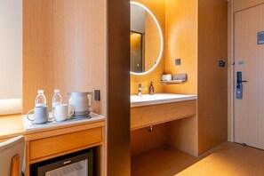 Une salle de bain moderne avec un meuble-lavabo en bois, un évier, un miroir avec un éclairage circulaire et une petite étagère contenant des articles de toilette.
