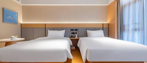 A hotel room with two beds, a bedside table with a lamp, a small table with a cup and saucer, and a painting on the wall.