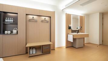 A modern hotel room with a wooden vanity, a bench with shoe storage, and a mirror above the sink.