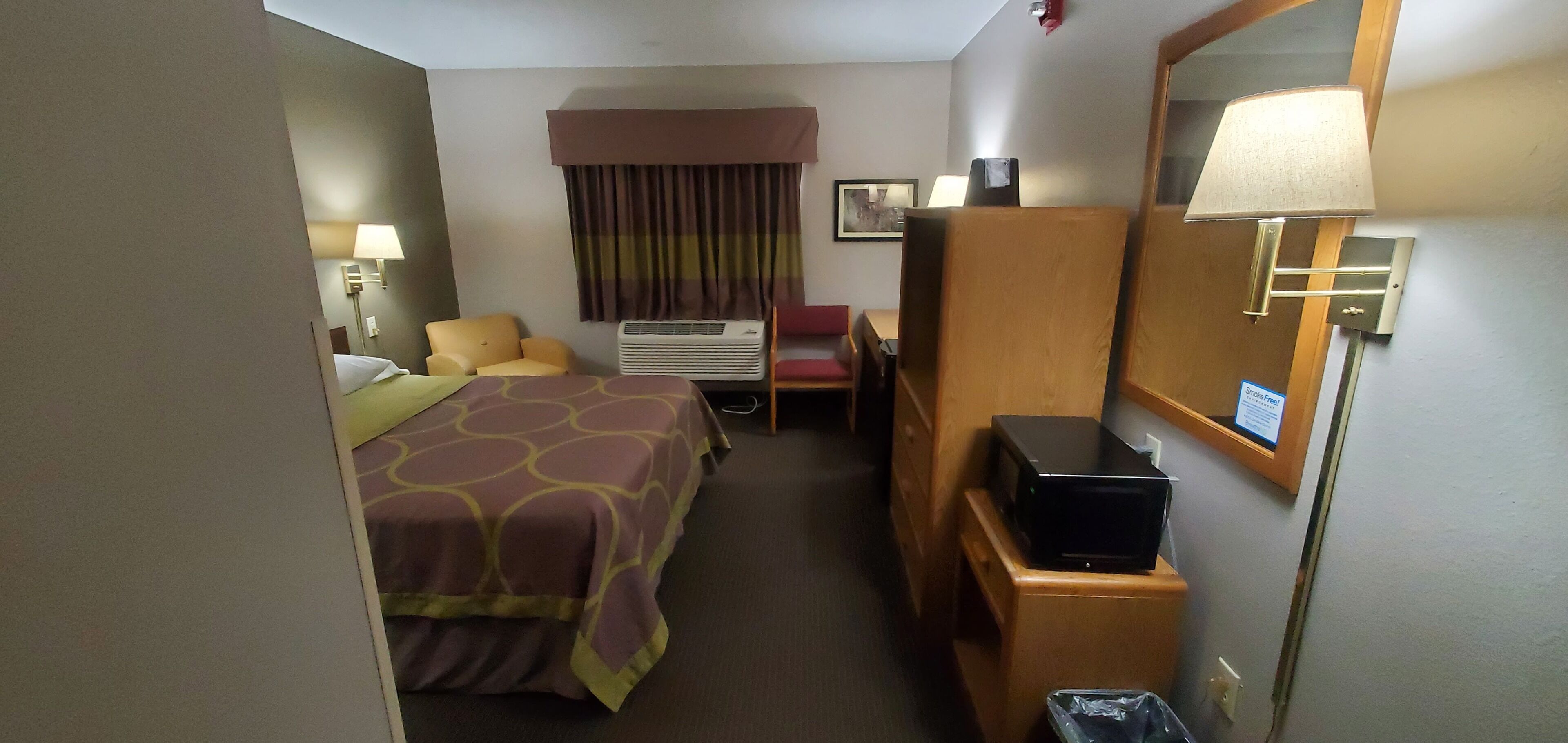 Una habitación de hotel con una cama, un escritorio, una silla, un televisor, aire acondicionado y una lámpara.