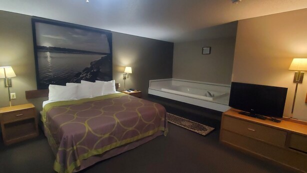 A hotel room with a bed, a TV, a bathtub, and two nightstands with lamps.