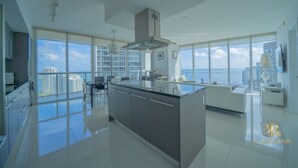 Eine moderne Küche mit großen Fenstern, einer zentralen Kochinsel und Blick auf Stadt und Meer.