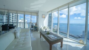 Ein geräumiges Wohnzimmer mit einem weißen Sofa, einem Couchtisch und großen Fenstern mit Blick auf die Stadt und das Wasser.