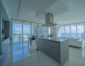 Une cuisine moderne dotée de grandes fenêtres, d’un îlot central et offrant une vue sur la ville et l’océan.