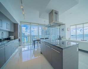 Une cuisine moderne dotée d’un grand îlot central, d’un coin repas et de grandes fenêtres offrant une vue sur la ville.