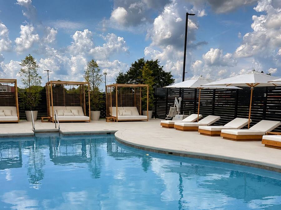 A pool area with lounge chairs and umbrellas, surrounded by a fence and trees.