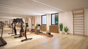 Un gimnasio amplio con equipo de ejercicio, pisos de madera, ventanas grandes y plantas en macetas.