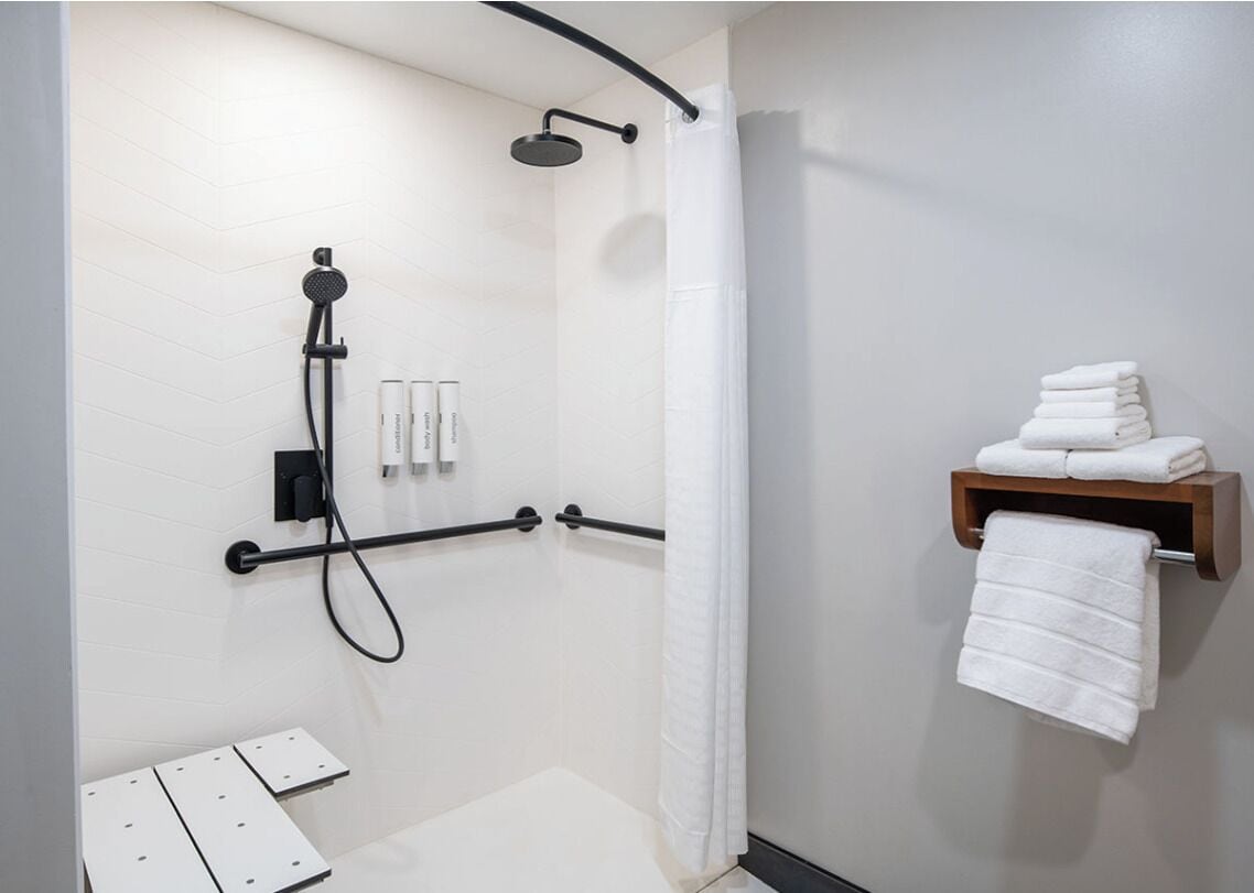 A modern bathroom with a shower, a towel rack, and a shelf with folded towels.