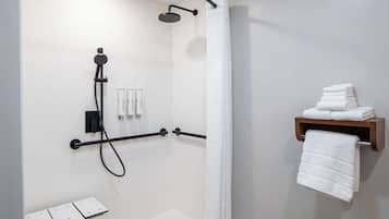 Um banheiro moderno com chuveiro, porta-toalhas e prateleira com toalhas dobradas.