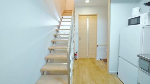 A staircase leading to a door, a kitchen area with a microwave, and a fire extinguisher on the floor. - Shinjuku Deep Lane White House・ZHUOJU (Tokyo)