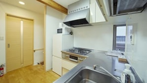 A compact kitchen with a gas stove, a microwave, and a built-in oven. There is a stainless steel sink and a window providing natural light. - Shinjuku Deep Lane White House・ZHUOJU (Tokyo)