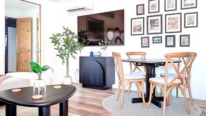 Ein modernes Wohnzimmer mit einem runden Tisch, Holzstühlen, einer Couch, einem Schrank und einer Wand voller gerahmter Kunstwerke.