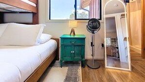 Ein Schlafzimmer mit einem Bett, einem grünen Nachttisch, einem Standventilator und einem Spiegel.