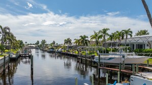 A marina with boats docked, a waterway, and a row of palm trees. - Turquoise Tides -Cape Coral (Cape Coral)