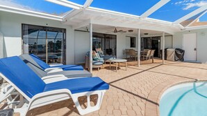 A covered outdoor area with lounge chairs, a pool, and a patio with tables and chairs. - Turquoise Tides -Cape Coral (Cape Coral)