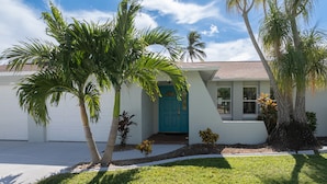 A single-story house with a teal front door, surrounded by palm trees and a well-maintained lawn. - Turquoise Tides -Cape Coral (Cape Coral)