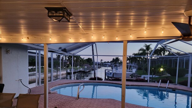 An outdoor pool area with a covered patio, seating, and a view of a marina. - Turquoise Tides -Cape Coral (Cape Coral)